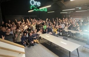 Collibrians gathered in the Brussels office, smiling and raising their hands beneath a glowing “One Collibra” sign.